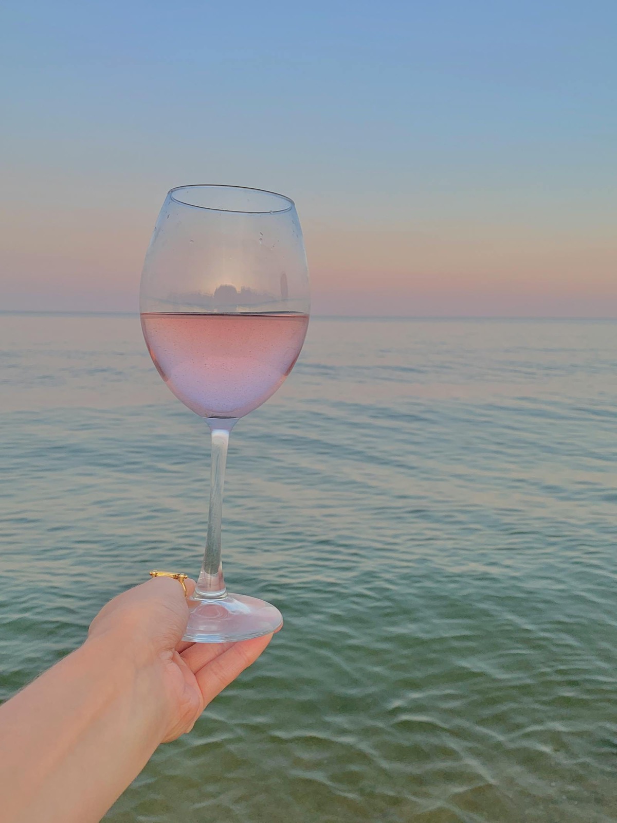Verre de rosé tenu devant la mer au coucher du soleil